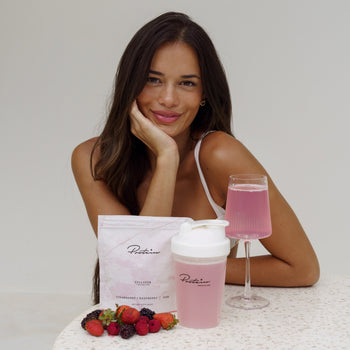 Woman sitting at a table with pink drink, berries, and a container labeled 'Puritane' on a white background.