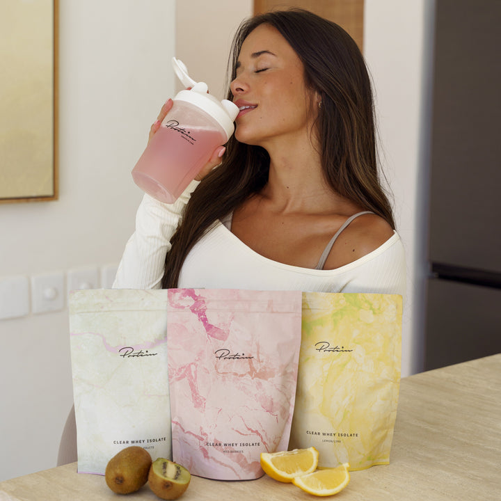 Woman drinking a pink smoothie from a shaker with Runtt packaging on a kitchen counter.